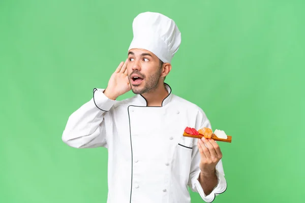 Joven Chef Caucásico Sosteniendo Sushi Sobre Fondo Aislado Escuchando Algo — Foto de Stock