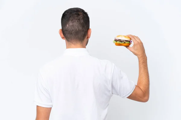 Młody Przystojny Biały Mężczyzna Trzymając Burger Nad Odizolowane Tło Tylnej — Zdjęcie stockowe