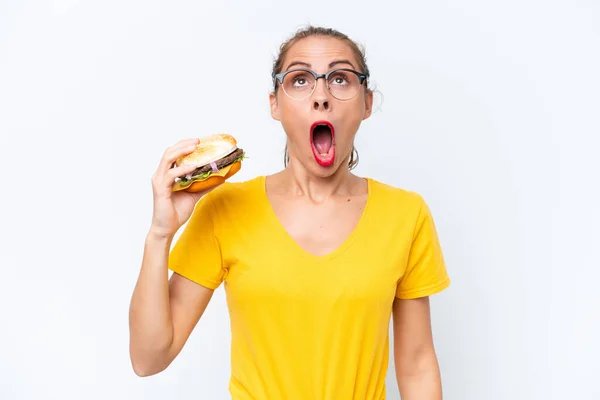 Młoda Kaukaska Kobieta Trzyma Hamburgera Izolowane Białym Tle Patrząc Górę — Zdjęcie stockowe