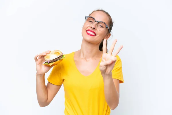 Młoda Kaukaska Kobieta Trzyma Hamburgera Odizolowany Białym Tle Szczęśliwy Liczyć — Zdjęcie stockowe