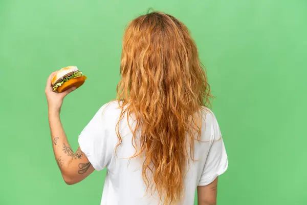 若いです白人女性を保持していますハンバーガー隔離上の緑の画面クロマキー背景で背部位置 — ストック写真