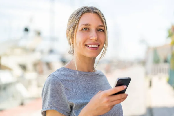Young Blonde Woman Using Mobile Phone Outdoors Smiling Lot — Stock Photo, Image