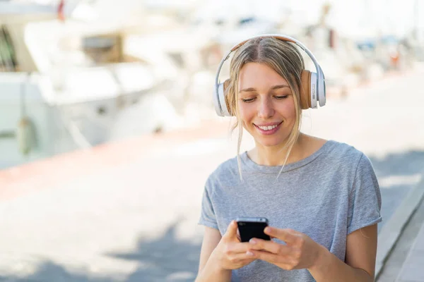 Giovane Donna Bionda All Aperto Ascoltando Musica Guardando Cellulare — Foto Stock