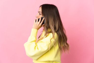Pembe arka planda izole edilmiş genç Romen kadın cep telefonuyla biriyle sohbet ediyor