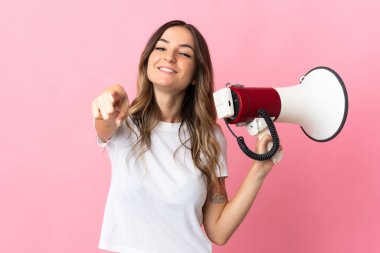 Pembe arka planda izole edilmiş genç Romen bir kadın elinde megafon, elinde gülümseyerek ön tarafı işaret ediyor.