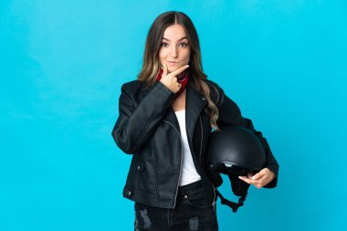 Elinde motosiklet kaskı tutan Romen kadın mavi arka planda izole edilmiş düşünüyor