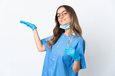 Romen kadın diş hekimi pembe arka planda izole edilmiş aletleri tutuyor ve davet edilmek için ellerini yana açıyor