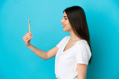 Mavi arka planda dişlerini fırçalayan beyaz kadın mutlu bir ifadeyle izole edilmiş.