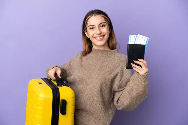 Stock image Young caucasian woman isolated on purple background in vacation with suitcase and passport