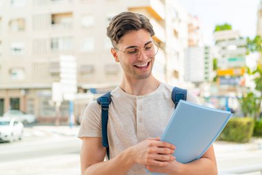 Genç ve yakışıklı bir öğrenci açık havada mutlu bir ifadeyle.