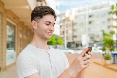 Genç yakışıklı adam cep telefonuyla mesaj ya da e-posta yolluyor.