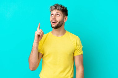 Mavi arka planda izole edilmiş yakışıklı beyaz adam yukarı bakıyor ve şaşırıyor.