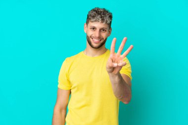 Mavi arka planda yalnız yaşayan yakışıklı beyaz adam mutlu ve parmaklarıyla üçe kadar sayıyor.