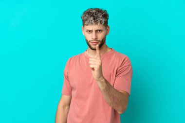 Mavi arka planda izole edilmiş yakışıklı beyaz adam hayal kırıklığına uğramış ve ön tarafı işaret ediyor.