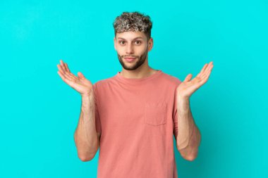 Mavi arka planda izole edilmiş yakışıklı beyaz adam şüpheli hareketler yapıyor.