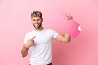 Pembe arka planda izole edilmiş yakışıklı beyaz bir adam boş bir levha tutuyor ve ona doğrultuyor.
