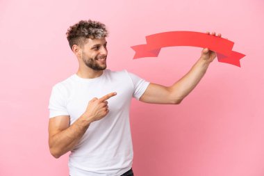Pembe arka planda izole edilmiş yakışıklı beyaz bir adam boş bir levha tutuyor ve ona doğrultuyor.