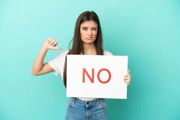 stock image Young caucasian woman isolated on blue background holding a placard with text NO and doing bad signal