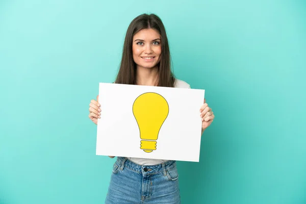 Young Caucasian Woman Isolated Blue Background Holding Placard Bulb Icon — Stock Photo, Image