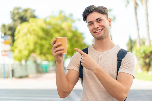 年轻英俊的男子在户外拿起咖啡 指着咖啡 — 图库照片