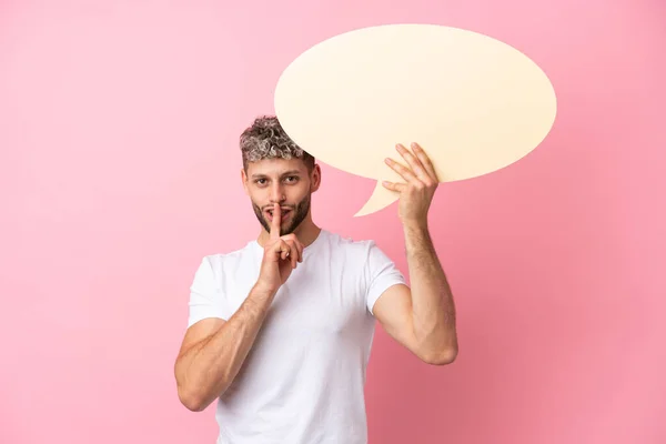 stock image Young handsome caucasian man isolated on pink background holding an empty speech bubble and doing silence gesture