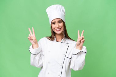 Genç aşçı beyaz kadın izole edilmiş geçmişinde zafer işaretini iki eliyle gösteriyor.