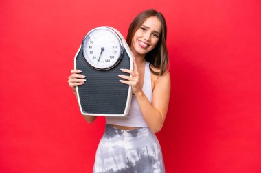 Güzel beyaz kadın, tartı makinesiyle kırmızı arka planda izole edilmiş.