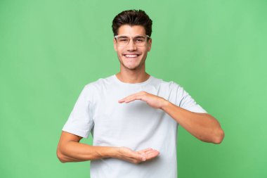 İzole edilmiş arka plan üzerinde genç beyaz yakışıklı bir adam bir ilan vermek için fotokopi makinesini avucunun içinde tutuyor.