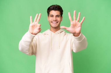 İzole edilmiş arka planda genç beyaz yakışıklı adam parmaklarıyla sekizi sayıyor.