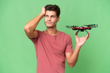 Kafkasyalı genç bir adam arka planda insansız hava aracı tutuyor. Şüpheleri var ve kafası karışık.