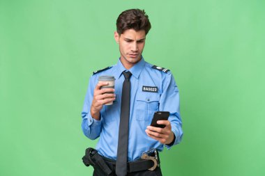 Arka planda izole edilmiş genç bir polis kahve ve bir cep telefonu tutuyor.