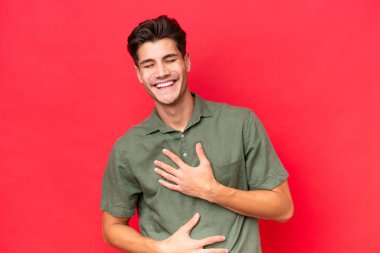 Kafkasyalı yakışıklı genç adam kırmızı arka planda izole edilmiş, gülümsüyor.