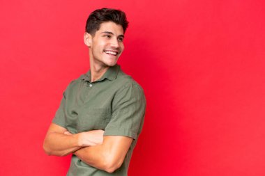 Genç, beyaz, yakışıklı bir adam kırmızı arka planda izole edilmiş, yana bakıyor ve gülümsüyor.