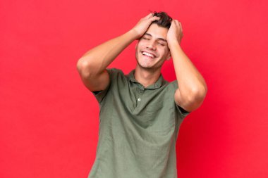 Kafkasyalı yakışıklı genç adam kırmızı arka planda izole edilmiş gülüyor.