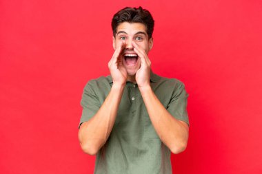 Beyaz tenli yakışıklı adam kırmızı arka planda izole edilmiş bağırıyor ve bir şeyler söylüyor.