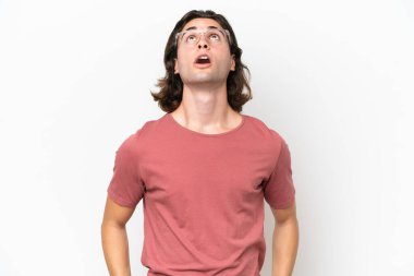 Beyaz arka planda soyutlanmış genç yakışıklı adam yukarı bakıyor ve şaşırmış bir ifadeyle
