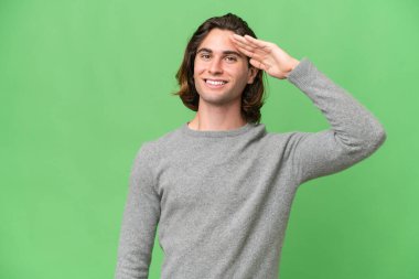 Yeşil krom arka planda izole edilmiş genç beyaz adam mutlu bir ifadeyle selamlıyor.