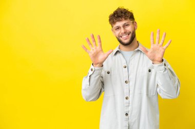 Sarı arka planda izole edilmiş yakışıklı beyaz adam parmaklarıyla ona kadar sayıyor.