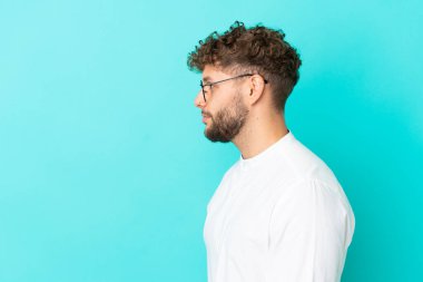 Mavi arka planda gözlüklü, yakışıklı, beyaz bir adam.