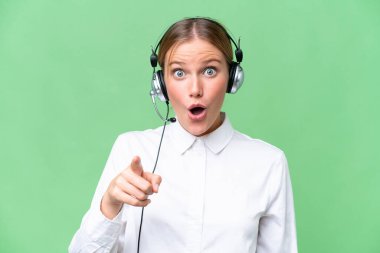 Tele pazarlamacı beyaz kadın izole bir geçmişi olan bir kulaklıkla çalışıyor şaşırmış ve ön tarafı işaret ediyor.