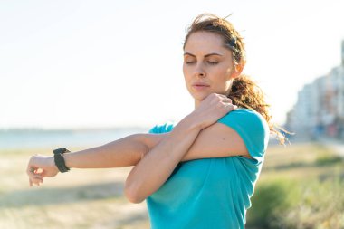 Dışarıda spor yapan ve esneme hareketleri yapan genç bir kadın.