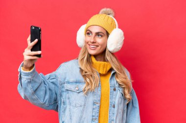 Genç ve güzel Uruguaylı kadın, kırmızı arka planda izole edilmiş kışlık kuklalar takıyor ve selfie çekiyor.