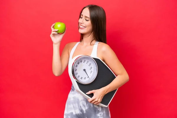 Young Beautiful Caucasian Woman Isolated Red Background Weighing Machine Apple — Stock Fotó