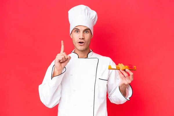 Joven Chef Caucásico Sosteniendo Sashimi Aislado Sobre Fondo Rojo Pensando — Foto de Stock