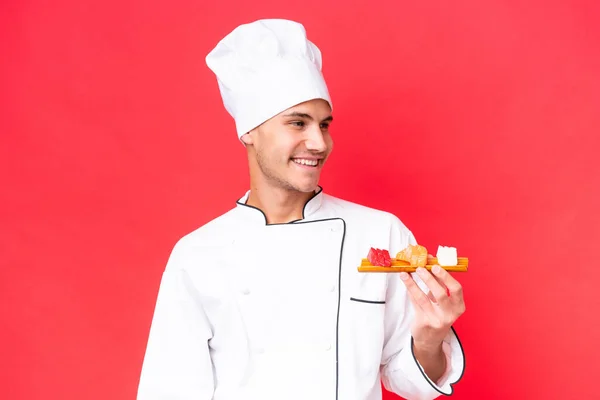 Jonge Kaukasische Chef Kok Met Sashimi Geïsoleerd Rode Achtergrond Kijken — Stockfoto