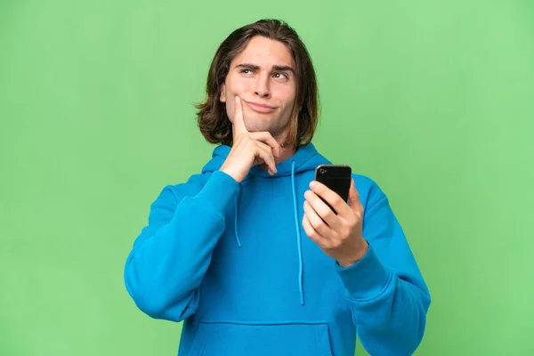 年轻英俊男子用手机和思维在绿色背景下被隔离 — 图库照片