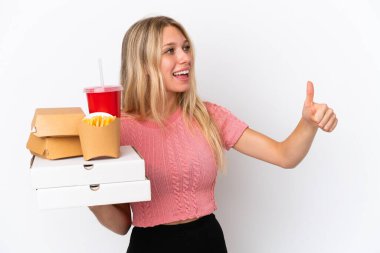 Mavi arka planda yağlı yiyecekler tutan beyaz bir kadın baş parmak işareti yapıyor.