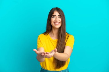 Mavi arka planda izole edilmiş genç beyaz kadın bir ilan vermek için avucunun içinde hayali bir fotokopi makinesi tutuyor.