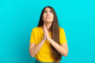 Mavi arka planda izole edilmiş genç beyaz kadın avuç içlerini bir arada tutuyor. İnsan bir şey ister.