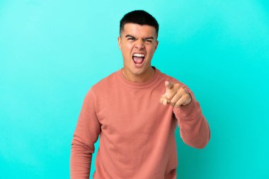 Soyutlanmış mavi arka plan üzerinde genç yakışıklı adam hayal kırıklığına uğramış ve ön tarafı işaret ediyor.